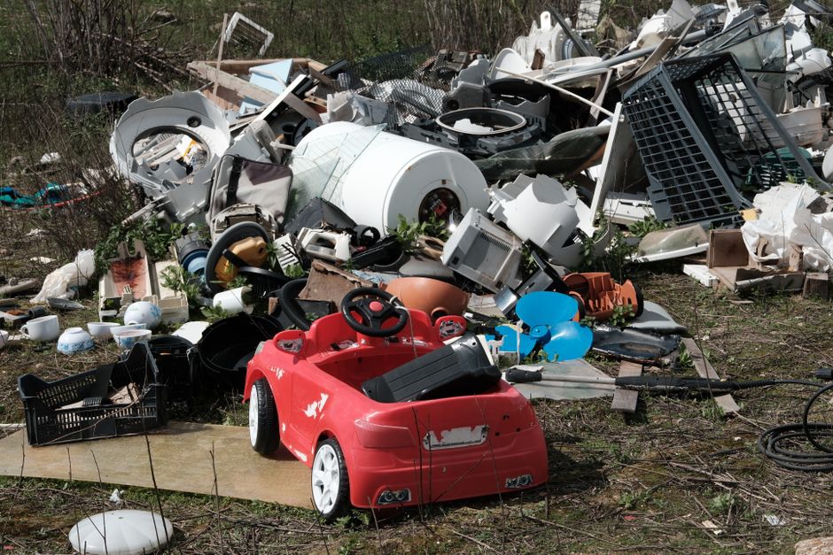 An extensive view of a large landfill site filled with mixed waste materials, including plastic wrappers, paper debris, food packaging, and discarded organic matter, spread across a wide area. The sur
